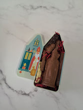 Afbeelding in Gallery-weergave laden, “Open Sinthuis-blik met chocolade Sinterklaas en andere chocoladefiguren, naast het deksel met sinterklaasprint.”