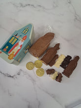Afbeelding in Gallery-weergave laden, “Inhoud van het Sinthuis met chocoladefiguren, goudkleurig verpakte chocolademunten en speculoos naast het huisvormige blik.”