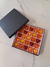 Load image into Gallery viewer, Close-up van ambachtelijke pralines: framboos-yoghurt, praliné brésilienne, hazelnootganache en caramel – luxe chocoladegarnituur