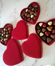 Load image into Gallery viewer, Close-up van ambachtelijke pralines: vanille, praliné, framboos en koffie, in fluwelen hartvormige doos