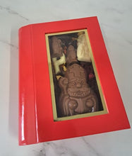 Load image into Gallery viewer, “Rode boekvormige geschenkdoos met gouden vensterrand en zichtbare chocoladefiguren van Sinterklaas.”
