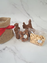 Load image into Gallery viewer, “Chocoladefiguren van Sinterklaas en Piet, chocolaatjes en nic-nackoekjes naast een jute zak met rode strik.”
