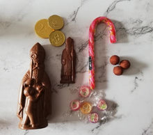 Load image into Gallery viewer, “Chocolade Sint, platte Sintfiguur, chocolademunten, marsepeinpatatjes, verpakte snoepjes en roze zuurstok op een lichte ondergrond.”
