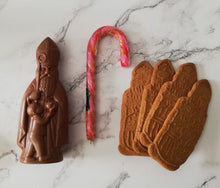 Load image into Gallery viewer, “Chocolade Sint naast een roze zuurstok en vier speculoosfiguren op een lichte gemarmerde ondergrond.”
